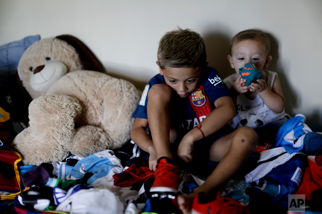 In this Jan. 25, 2017 photo, Benjamin Palandella puts on his soccer shoes as he sits with his little brother Bautista Lionel and his stuffed toys on his bed in Buenos Aires, Argentina. "I want to be like Messi and play for Barcelona," said Palandella. He likes how the Barcelona star "steps" on the ball, scores and shoots free kicks. (AP Photo/Natacha Pisarenko)