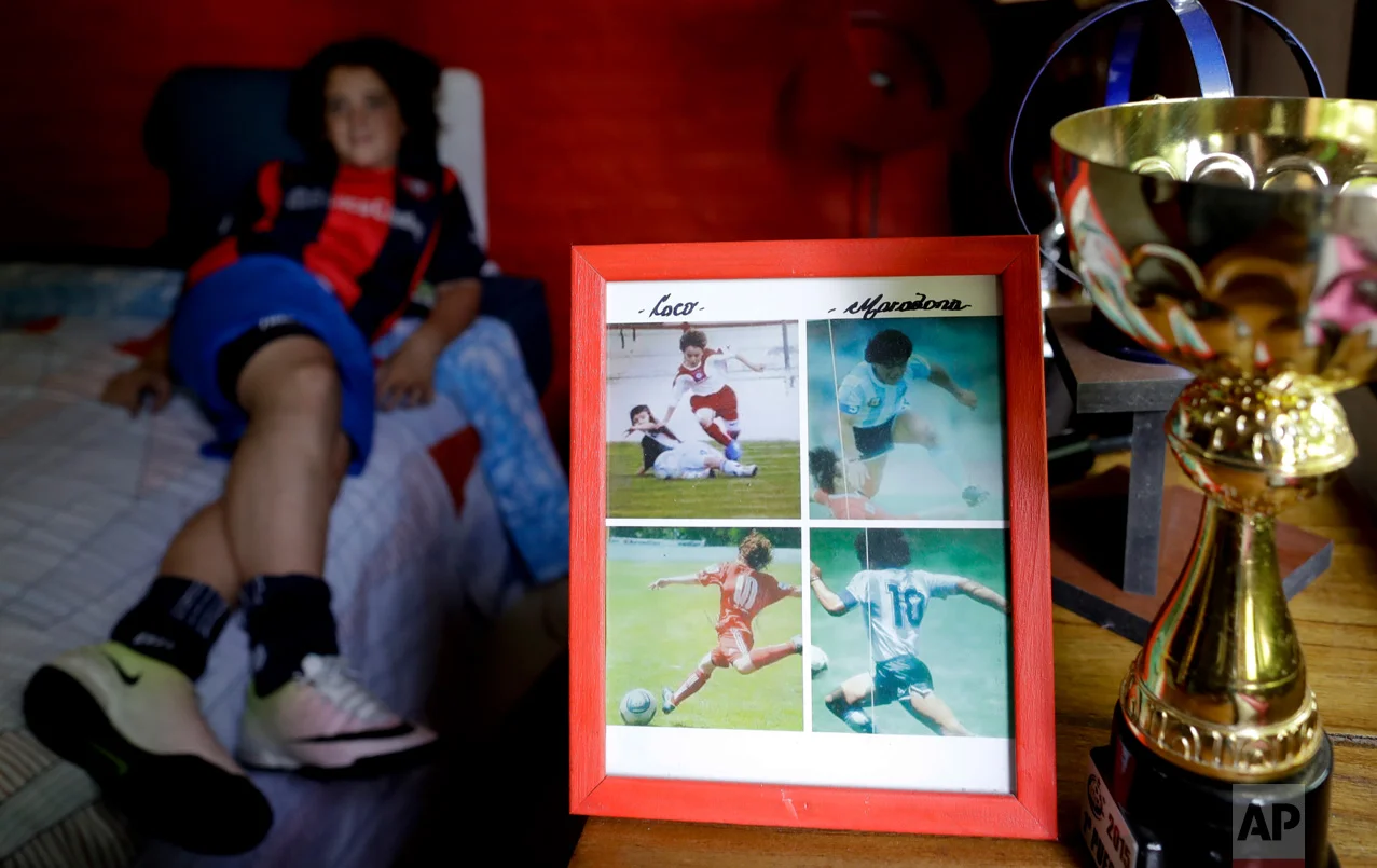 In this Nov. 19, 2016 photo, a framed picture shows Thiago "Coco" Perugini next to images of soccer star Diego Maradona, at his home where he lies on bed, on the outskirts of Buenos Aires, Argentina. Like Maradona, Thiago is a classic playmaker. He knows that he wants to be a professional soccer player. But what would he do, if he doesn't end up going pro? After a long silence, he shrugs his shoulders, smiles and answers: "I don't know." (AP Photo/Natacha Pisarenko)