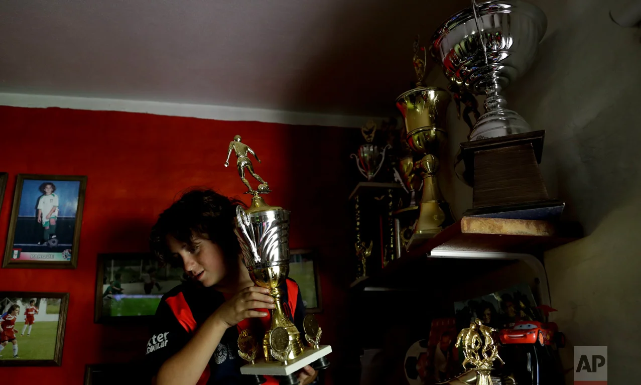 In this Nov. 19, 2016 photo, Thiago "Coco" Perugini shows one of his trophies to journalists inside his room on the outskirts of Buenos Aires, Argentina. Thiago recently transferred to the youth division of San Lorenzo and his parents had his wall painted in the club's red and blue colors. (AP Photo/Natacha Pisarenko)