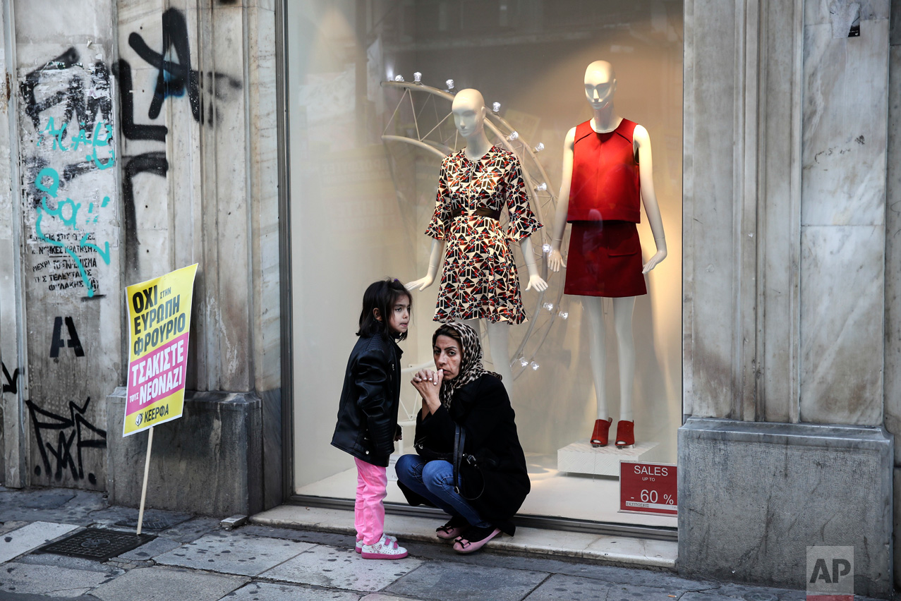 A refugee and her daughter sit next to a placard in front of a shop window during a rally in Athens, Saturday, March 18, 2017. Thousands of protesters marched to the offices of the European Commission Representation in Greece to mark the United Nations' Anti-Racism Day. The placard reads: "No to a fortress-Europe, Crush the Neo-Nazis". (AP Photo/Yorgos Karahalis)