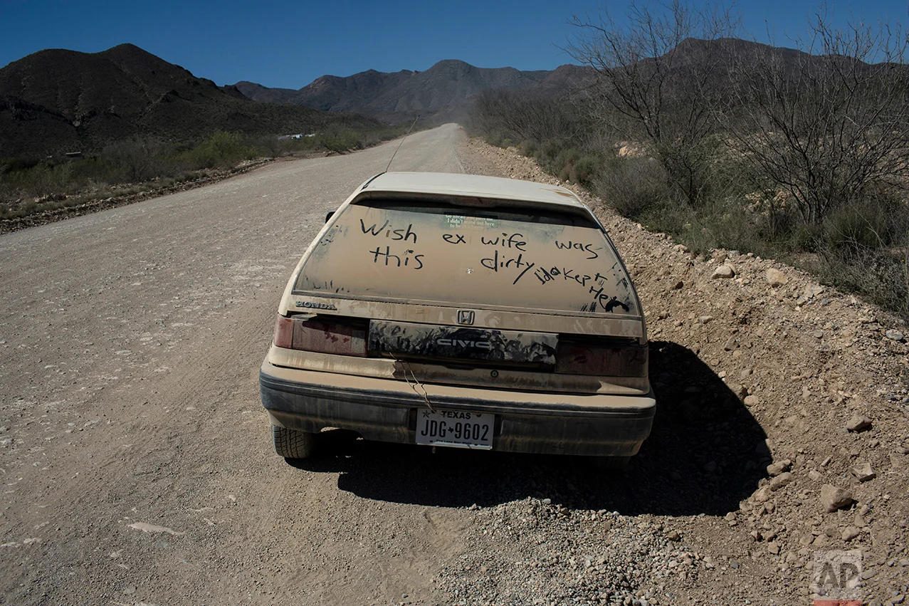 A car with a message written on its dusty back window sits abandon on the side of a road in Terlingua, Texas, near the US-Mexico border, Monday, March 27, 2017. (AP Photo/Rodrigo Abd)