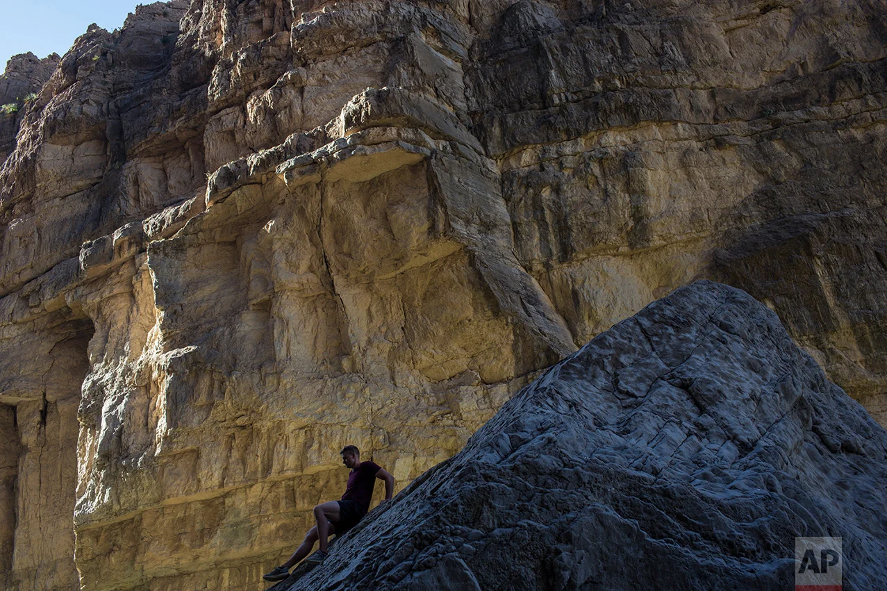 A man descends a rock on the bank of the Rio Grande river, just feet from a cliff face that is Mexico, in Santa Elena Canyon as he vacations at Big Bend National Park in Texas, Monday, March 27, 2017. (AP Photo/Rodrigo Abd)