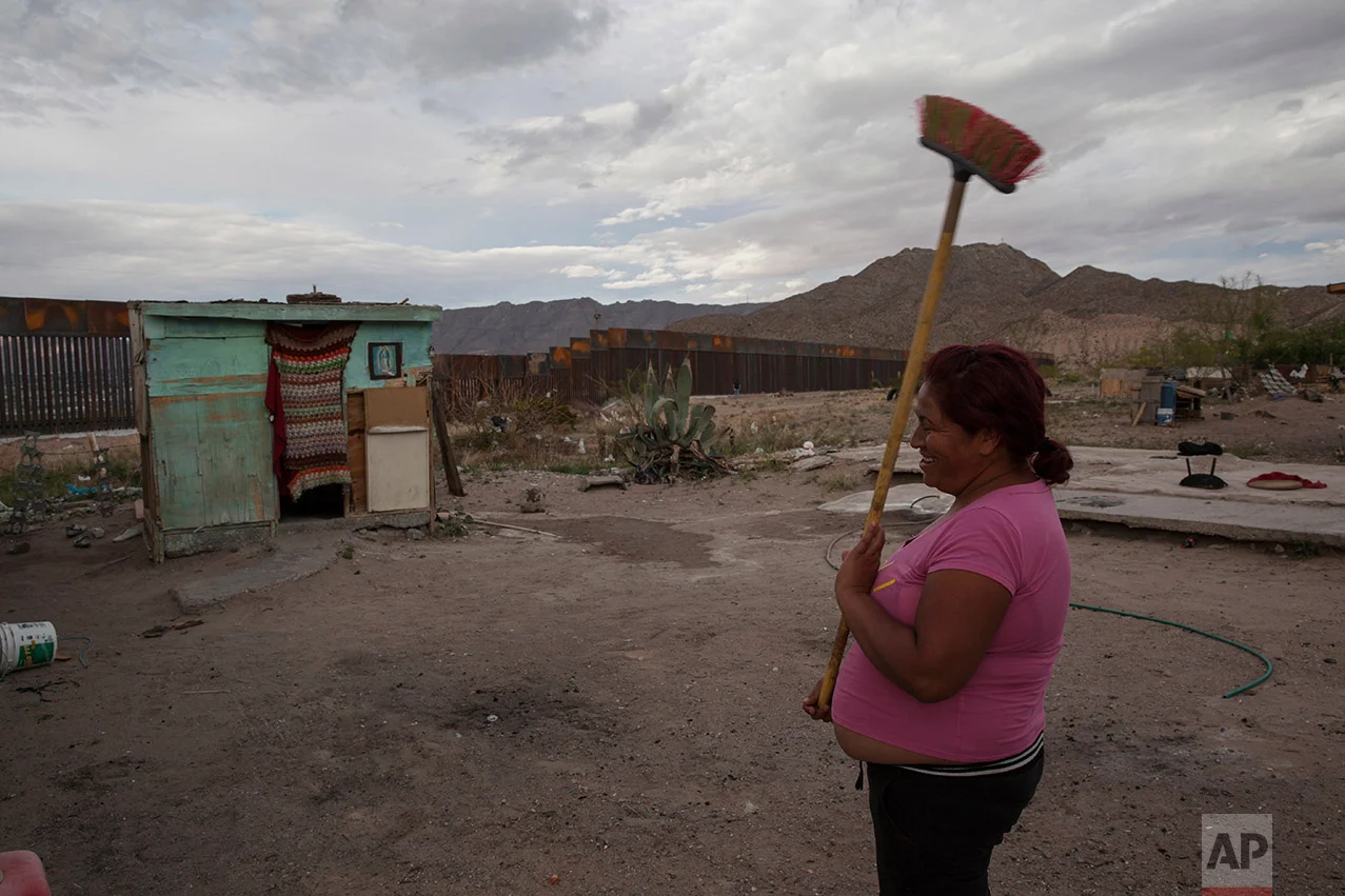 Claudia Sanchez holds a broom outside her shack home in the Anapra neighborhood of Ciudad Juarez, Mexico, Wednesday, March 29, 2017, across the border from Sunland Park, New Mexico. Homes in this area are made of concrete block, wooden pallets, and any sort of recovered material that can withstand the wind and hold back the blowing sand of the dunes. (AP Photo/Rodrigo Abd)