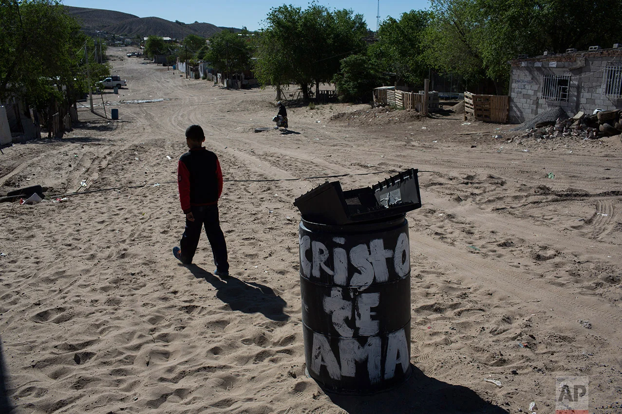 A boy walks away from the municipal garbage dump where he threw away the casing of an unusable TV, in the Anapra neighborhood of Ciudad Juarez, Mexico, Thursday, March 30, 2017, across the border from Sunland Park, New Mexico. The trash can reads in Spanish "Christ loves you." (AP Photo/Rodrigo Abd)