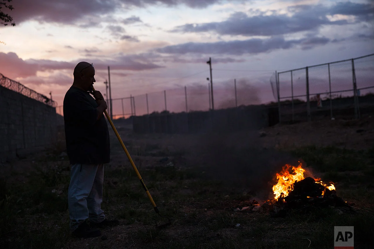 A man burns trash near the border fence in the Anapra neighborhood of Ciudad Juarez, Mexico, late Wednesday, March 29, 2017, across the border from Sunland Park, New Mexico. Residents of Anapra, a neighborhood anchored to the dunes, have fought to get running water, electricity and some paved streets in recent years. (AP Photo/Rodrigo Abd)