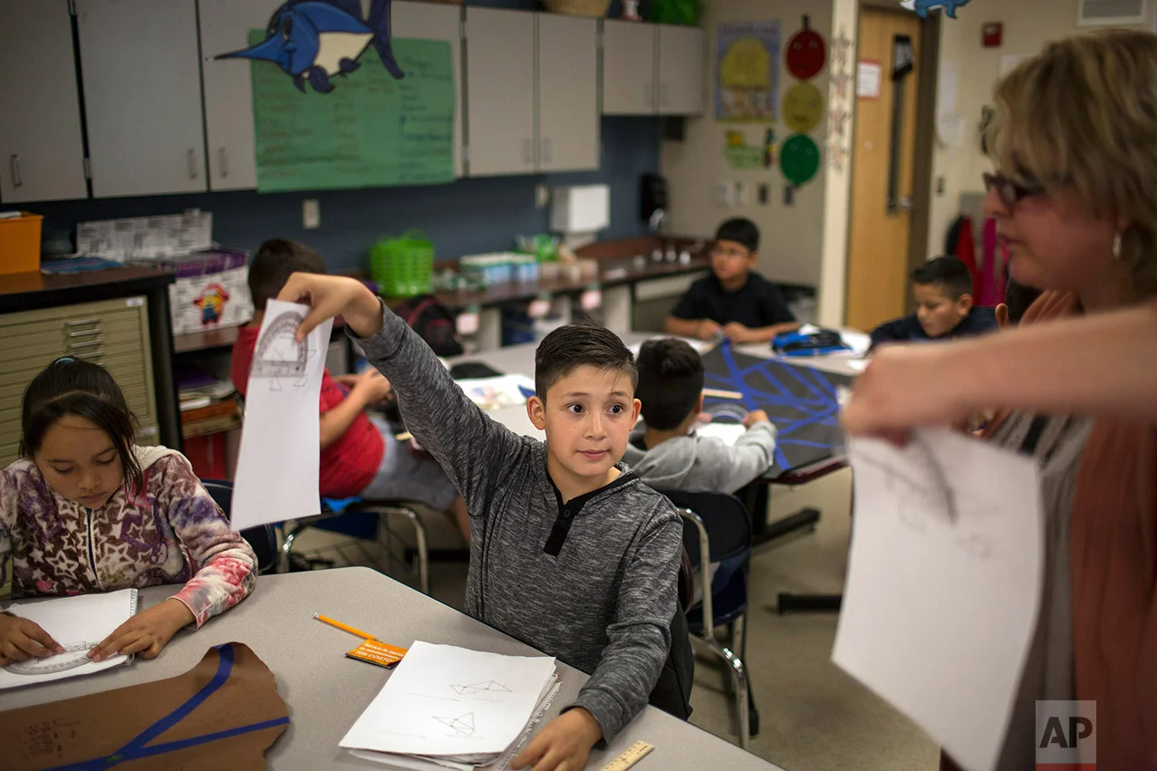 A fifth grade student shows his geometry work to a teacher at Columbus Elementary School, in Columbus, New Mexico, Friday, March 31, 2017. (AP Photo/Rodrigo Abd)