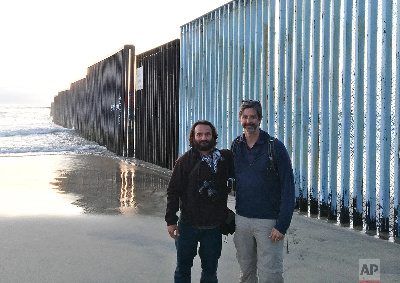 In this Tuesday, April 4, 2017 photo, Associated Press photographer Rodrigo Abd and correspondent Christopher Sherman, pose for a photo at the end of their 3,000 mile journey, backdropped by the US-Mexico border fence that separates Tijuana, Mexico, from San Diego, Calif. (AP Photo)