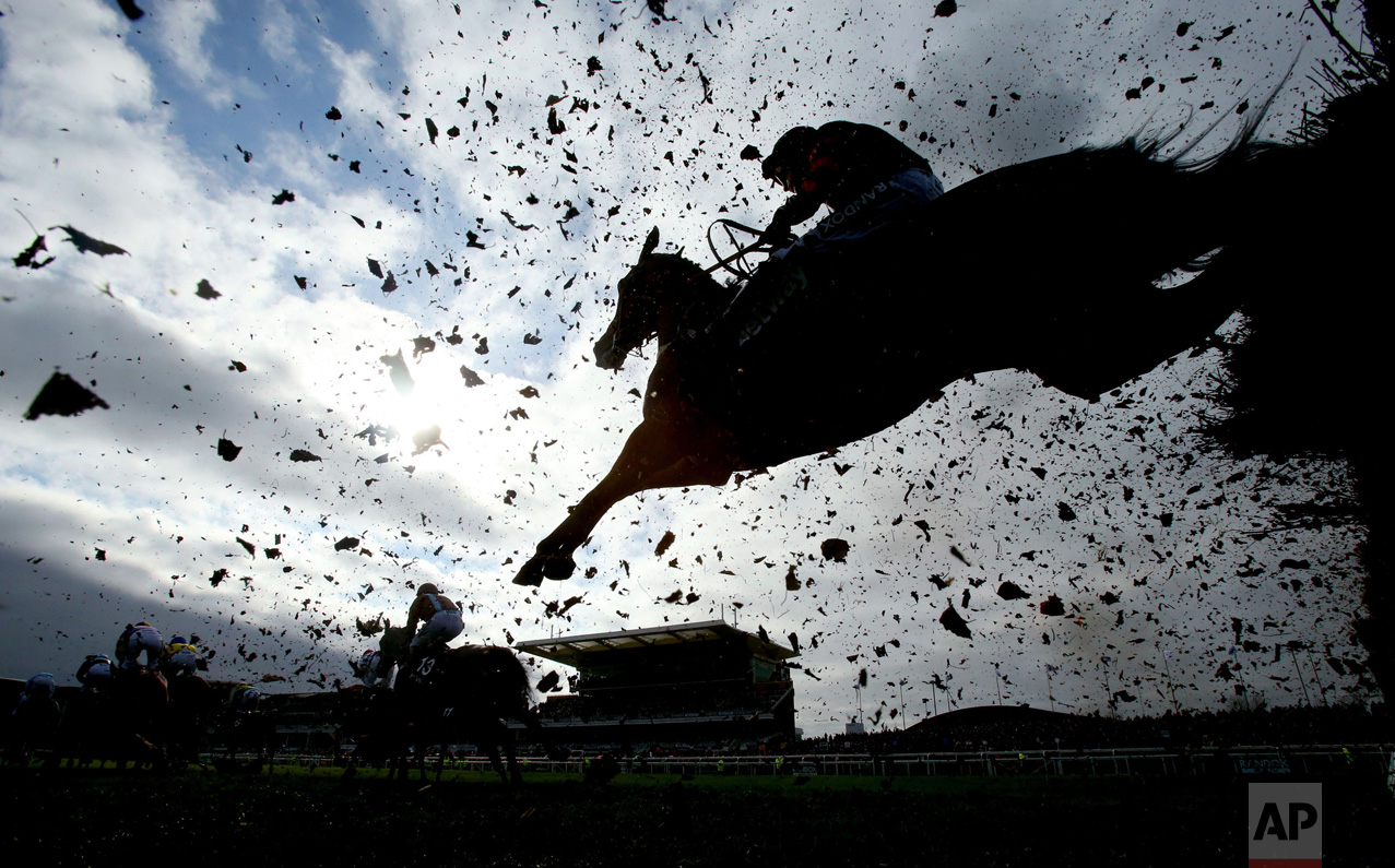 Debris flies as runners and riders clear a fence during the first day of the Grand National Festival at Aintree Racecourse, England, on Thursday April 6, 2017. (Niall Carson/PA via AP)