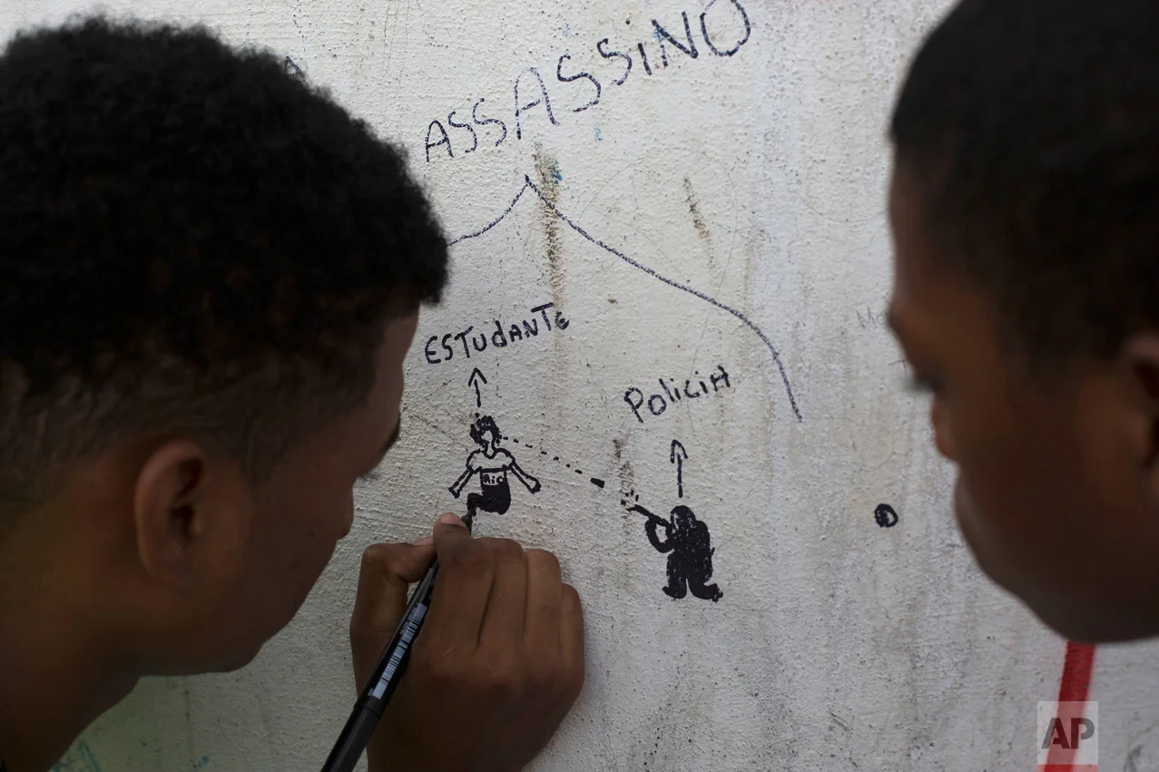 In this March 31, 2017 photo, a boy makes a drawing depicting a police officer shooting at a student on the wall of the school where 13-year-old girl Maria Eduarda Conceicao was killed by a stray bullet during a shootout between police and alleged drug traffickers, in Rio de Janeiro, Brazil. Large bullet holes can still be seen on the school's outer wall and front gate, a grim reminder for students, teachers and parents walking in every day. (AP Photo/Leo Correa)