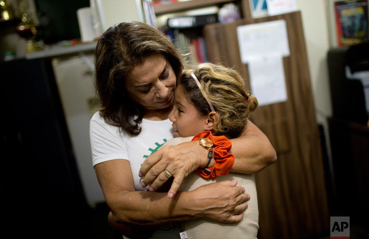 In this April 5, 2017 photo, Yvonne Bezerra de Mello embraces a girl in the Uere school at the Mare slum in Rio de Janeiro, Brazil. "After (a shootout) it's not possible to teach," said Bezerra de Mello, the founder of Uere, which offers classes for underprivileged students with learning difficulties. "So we just play and talk, because some of the children get really nervous." (AP Photo/Silvia Izquierdo)