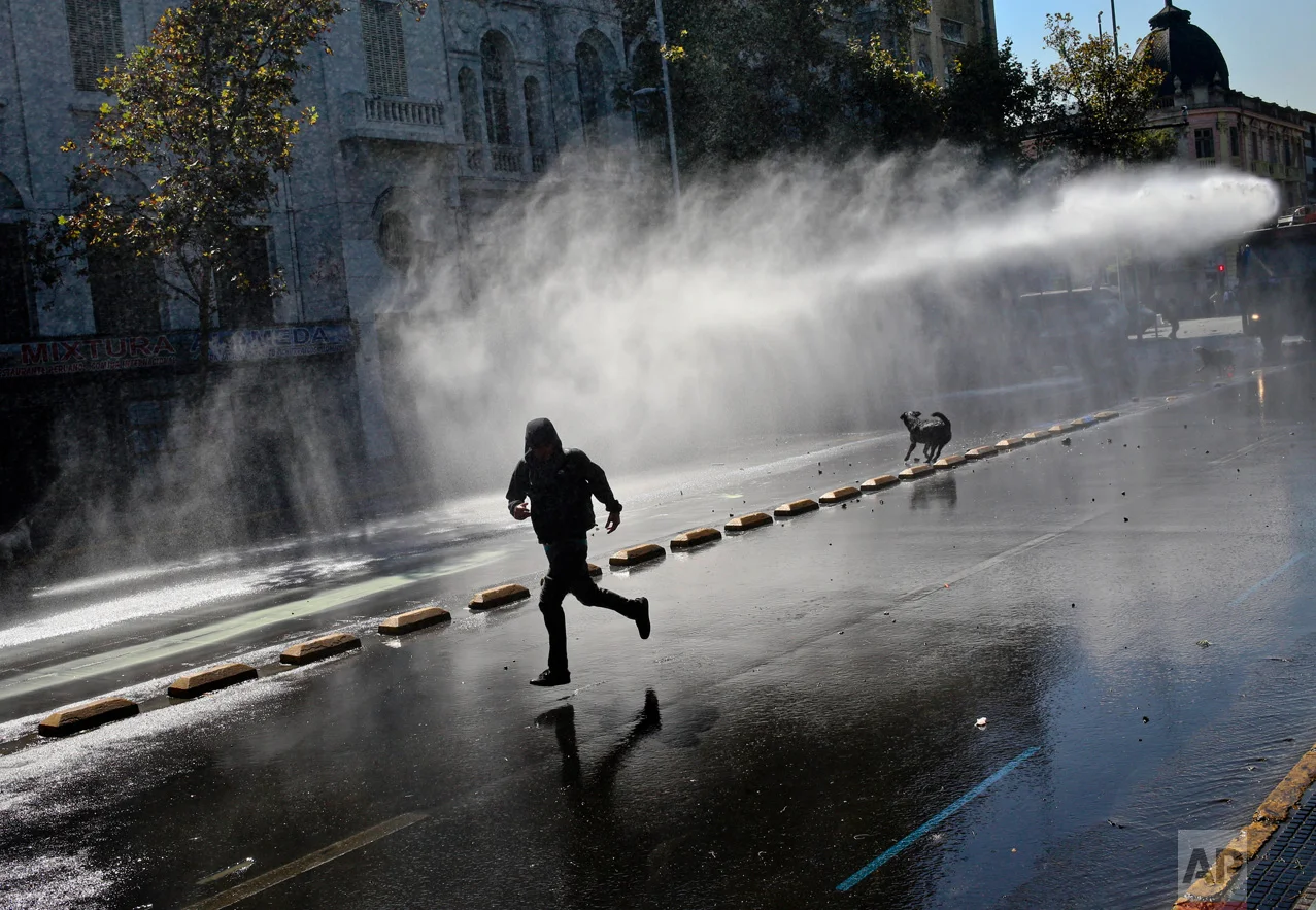 A demonstrator runs for cover as police fire a water cannon during a protest demanding education reform in Santiago, Chile, Tuesday, April 11, 2017. The demonstrators are demanding free access to school for all ages, including the university level. (AP Photo/Esteban Felix)
