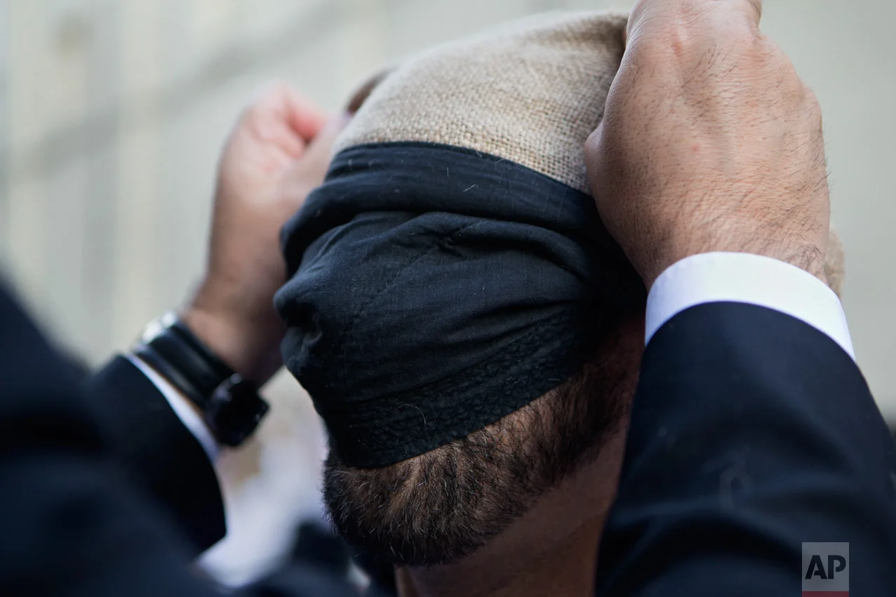 In this Thursday, April 13, 2017 photo, a 'Costalero' gets help to attach a sackcloth to protect his head before the start of a Holy Week procession during a Holy Week procession in Madrid, Spain. (AP Photo/Paul White)