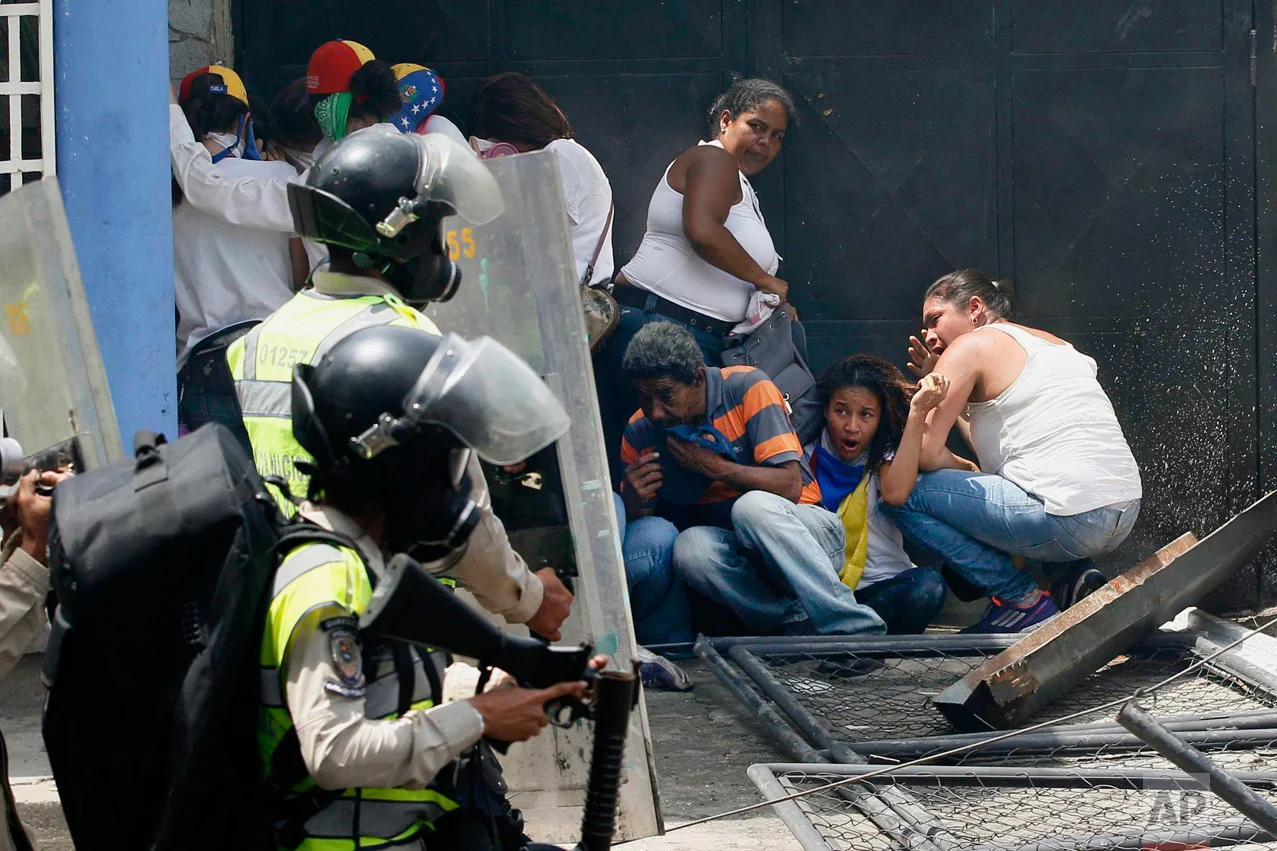 Anti-government demonstrators take cover from advancing Bolivarian Police officers during protests in Caracas, Venezuela, on Wednesday, April 19, 2017. Opponents of President Nicolas Maduro called on Venezuelans to take to the streets in marched against the embattled socialist leader. (AP Photo/Ariana Cubillos)