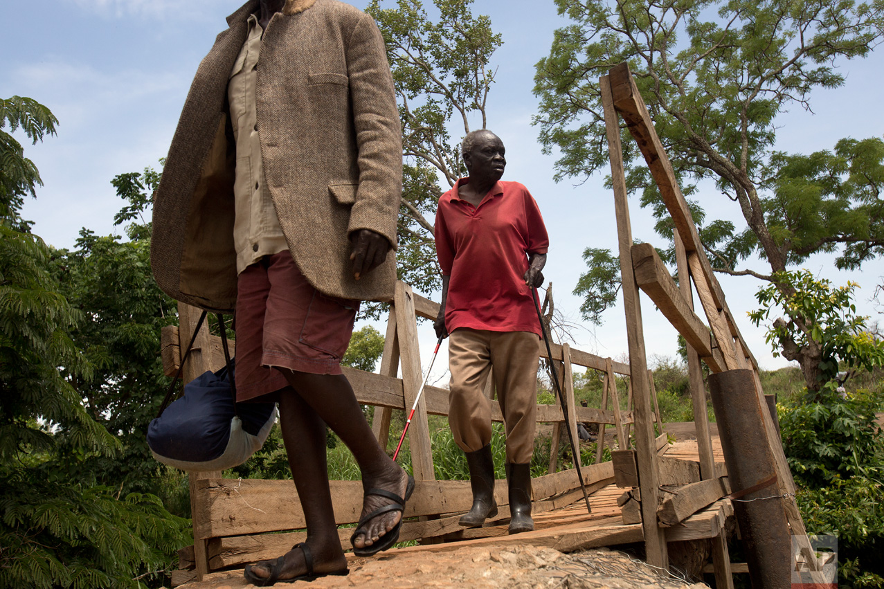 In this Wednesday March 29, 2017 photo, Ringo Gwiya, 80, a blind South Sudanese refugee, crosses the bridge over the Kaya River linking South Sudan to Uganda near Busia. (AP Photo/Jerome Delay)