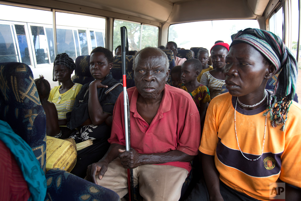 In this Wednesday March 29, 2017 photo, Jenifer Juan, daughter of Alfred Wani, sits next to Ringo Gwiya, center, in a minibus after being processed by U.N. officials in Busia, Uganda. They were later transported to the Kuluba transit camp. (AP Photo/Jerome Delay)