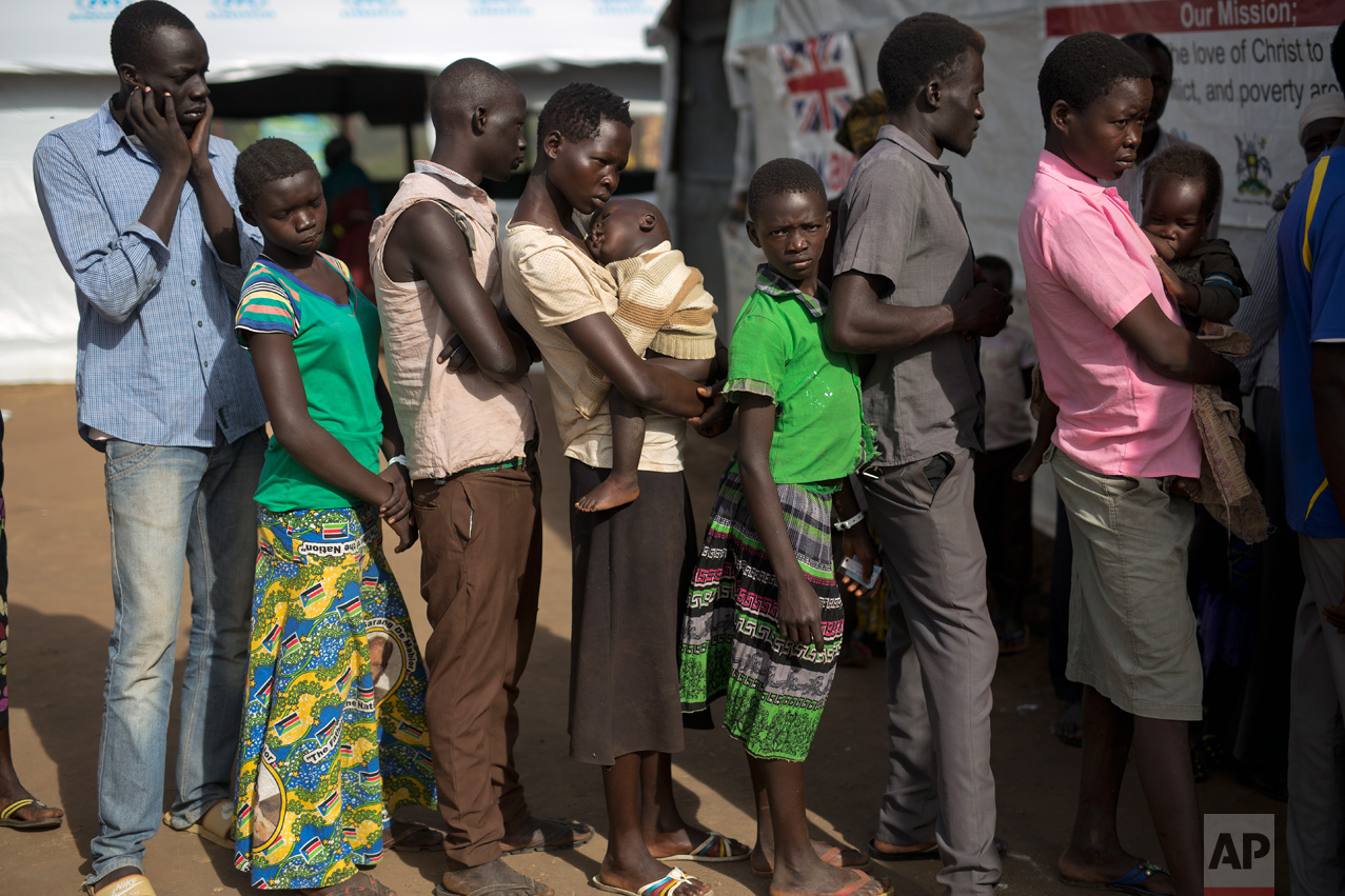 In this Thursday March 30, 2017 photo, South Sudanese refugee Mary Kide and her son, Desem, stand in line with others, including Samson Tabani, left, to get a medical check up at the Kuluba transit camp. (AP Photo/Jerome Delay)