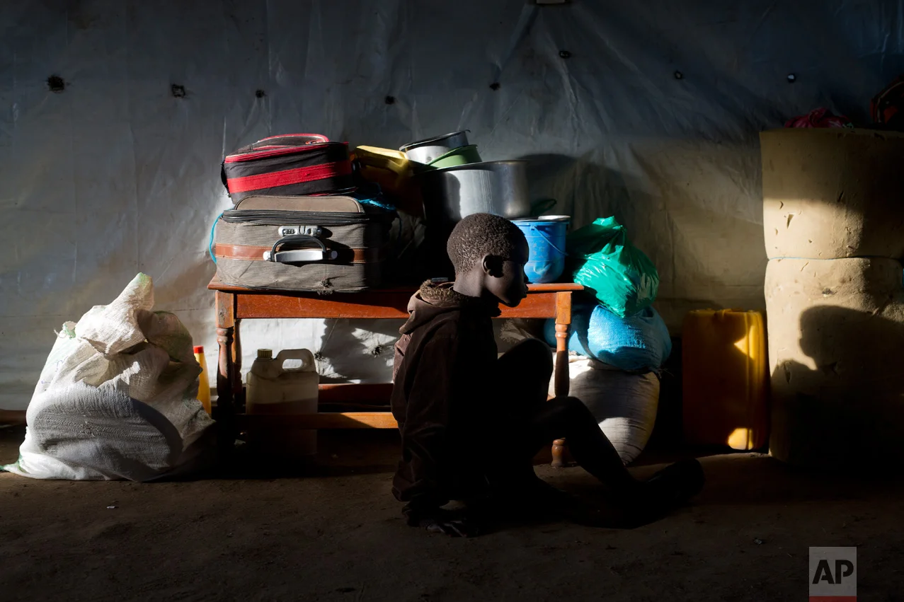 In this Friday March 31, 2017 photo, Daniel Kampa, 8, sits in a ray of light by his suitcase in a communal tent at the Kuluba, Uganda, transit camp, waiting for transport to the Imvepi camp. (AP Photo/Jerome Delay)