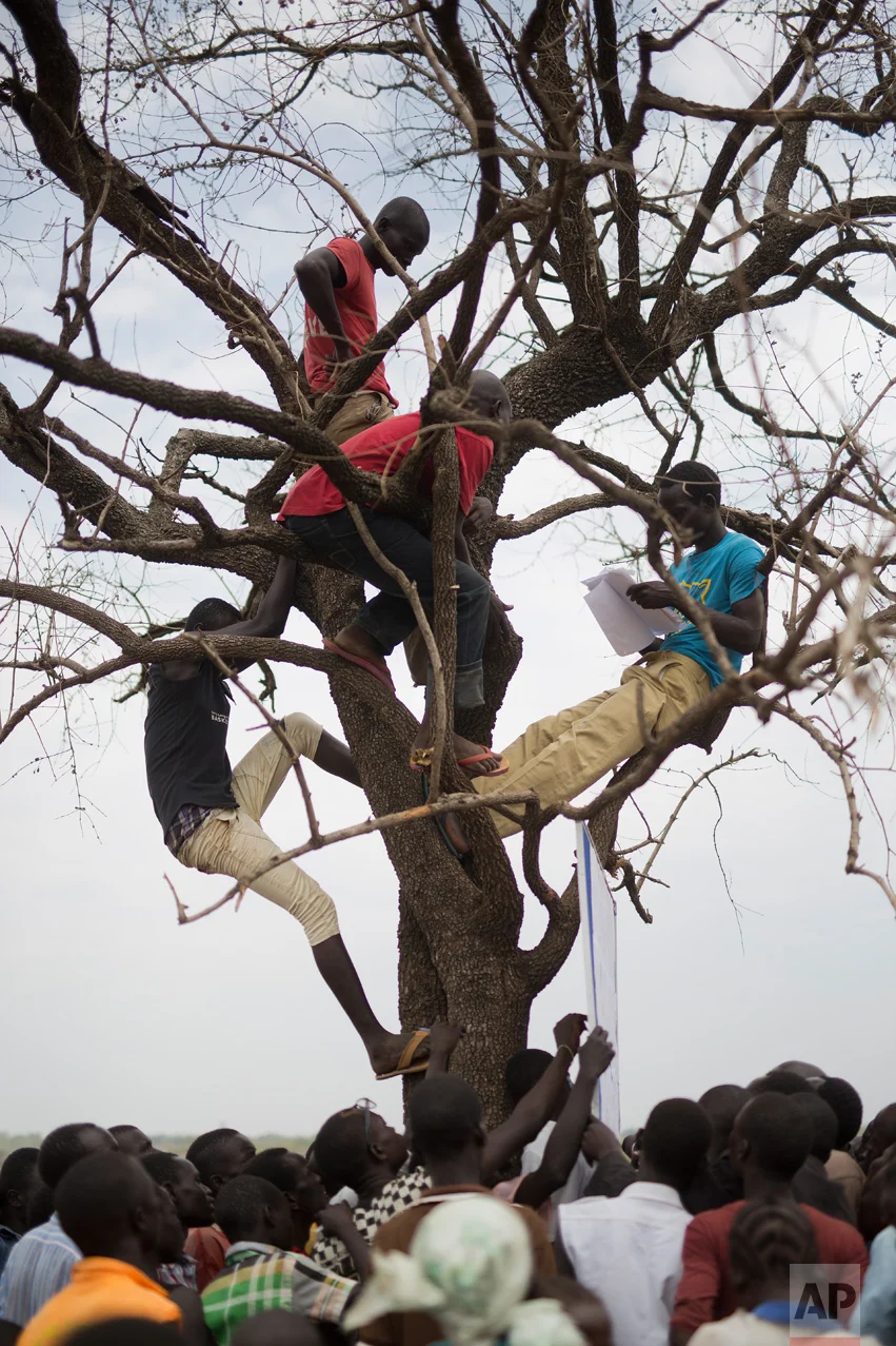 In this Monday, April 3, 2017 photo in the Imvepi camp, South Sudanese refugees gather under a tree from which names are announced for those allocated a land parcel from the Ugandan government. (AP Photo/Jerome Delay)