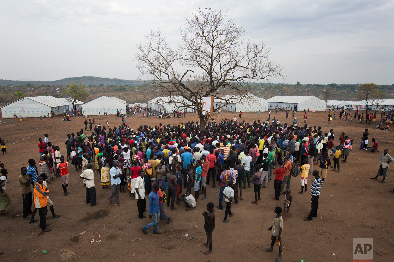 In this Monday, April 3, 2017 photo in the Imvepi camp, South Sudanese refugees gather under a tree from which names are announced for those allocated a land parcel from the Ugandan government. (AP Photo/Jerome Delay)