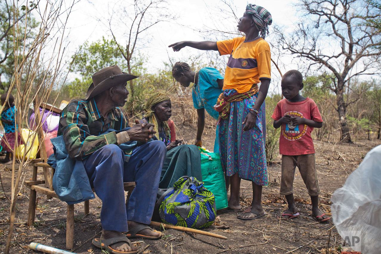 In this Tuesday, April 4, 2017 photo in the Imvepi camp, Jenifer Juan points at children as her parents, Alfred and Kassa Wani rest on chairs after traveling by truck to the plots of land they were allocated by the Ugandan government for their resettlement. Imvepi is growing at a rate of over 2,000 refugees each day. (AP Photo/Jerome Delay)