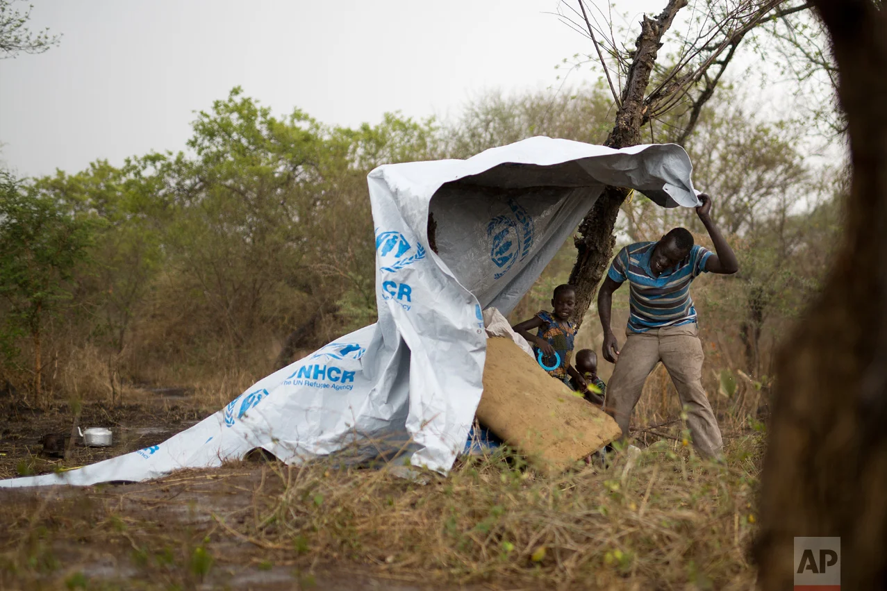 In this Wednesday, April 5, 2017 photo in the Imvepi camp, Samson Wani grabs a flapping plastic cover during a rain storm on the plot of land he and family were allocated by the Ugandan government for their resettlement. (AP Photo/Jerome Delay)