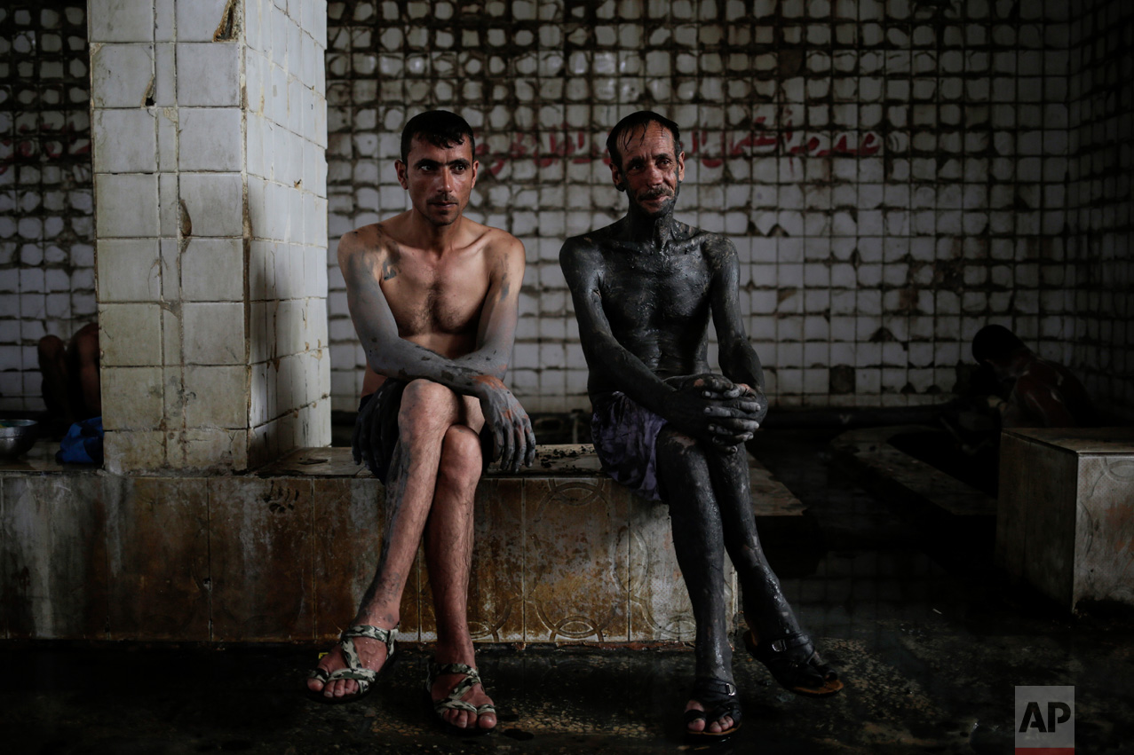 Two customers of the Hamam Alil spa south of Mosul, Iraq, take a break from bathing after covering themselves with mud from a nearby sulphur well, Thursday, April 27, 2017. The mud is supposedly healthy for the skin. (AP Photo/Bram Janssen)