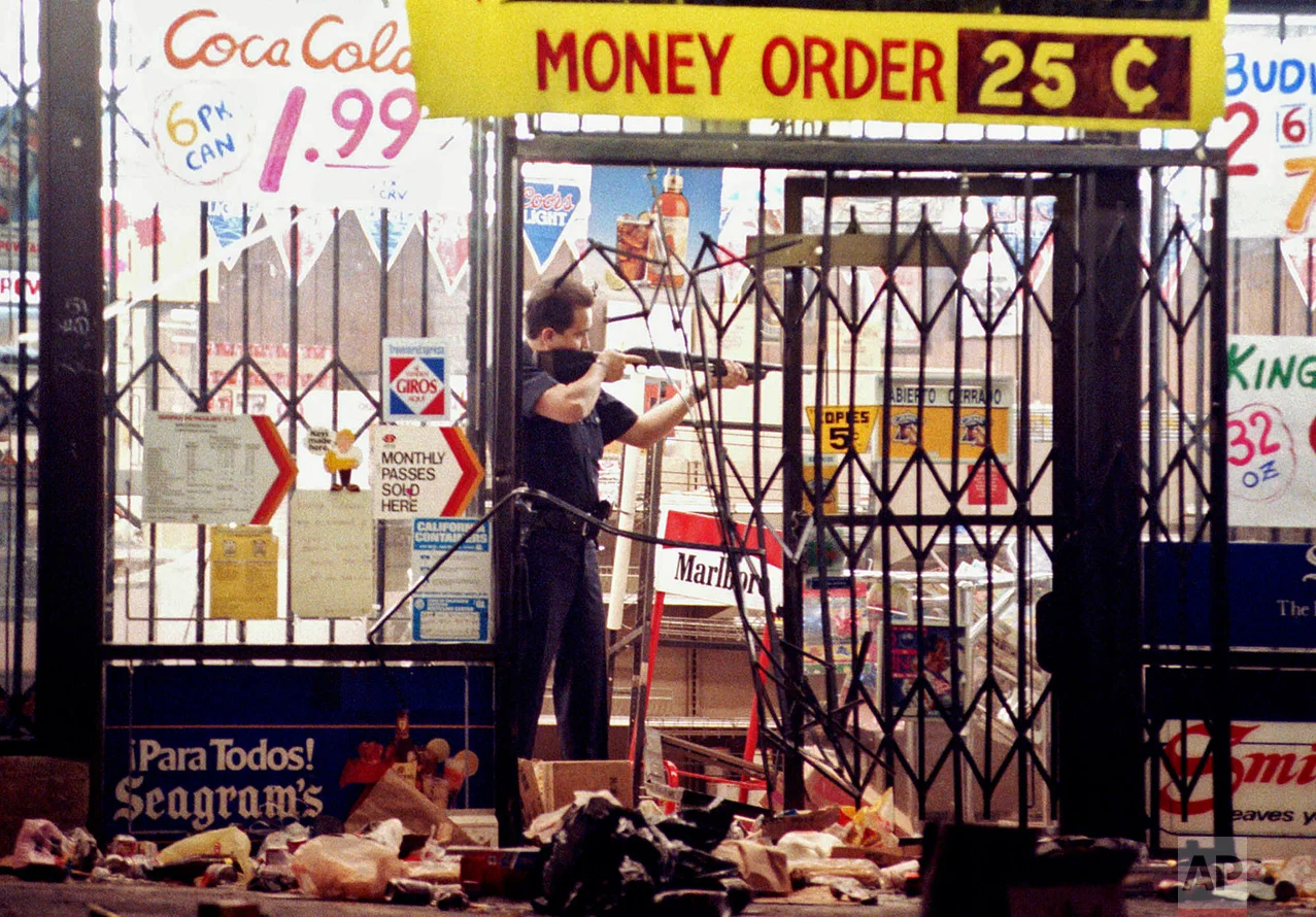 In this April 30, 1992 photo, a Los Angeles police officer takes aim at a looter in a market at Alvarado and Beverly Boulevard in Los Angeles during the second night of rioting in the city. (AP Photo/John Gaps III)