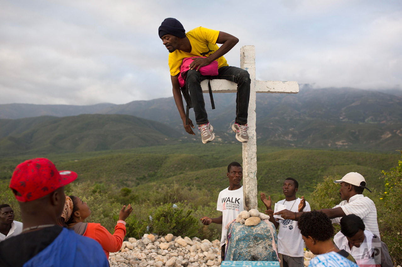 Haitians gather at the 14th station of the cross around a man sitting on the horizontal bar of the cross, who they believe has been taken over by a voodoo spirit, during the annual Good Friday pilgrimage to the mount Calvaire Miracle, in Ganthier, Haiti, Friday, April 14, 2017. (AP Photo/Dieu Nalio Chery)