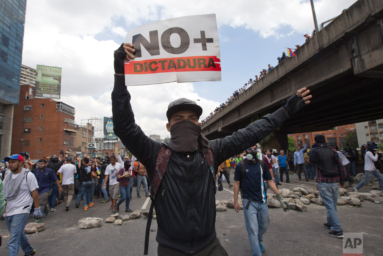 A demonstrator holds up a sign that reads in Spanish read "No more dictatorship" during a protest in Caracas, Venezuela, Thursday, April 6, 2017. The South American country has seen near-daily protests since the Supreme Court issued a ruling nullifying congress last week. The court pulled that decision back after it came under heavy criticism, but opposition leaders said the attempt to invalidate a branch of power revealed the administration's true dictatorial nature. (AP Photo/Ariana Cubillos)