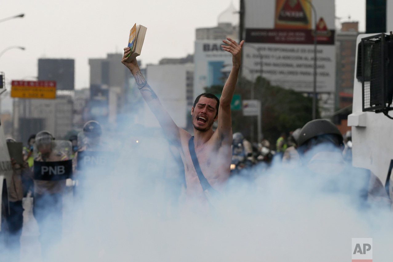 An anti-government protester holds a bible in the middle of a cloud of tear gas during a march in Caracas, Venezuela, Thursday, April 20, 2017. Tens of thousands of protesters flooded the streets again, one day after three people were killed and hundreds arrested in the biggest anti-government demonstrations in years. (AP Photo/Fernando Llano)