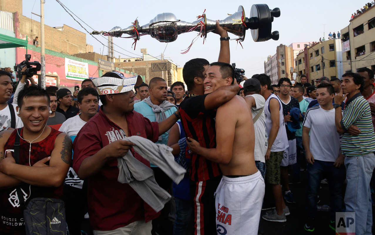  In this Monday, May 1, 2017 photo, a fan of the "Purito Barrios Altos" soccer team holds high his team's trophy as he hugs a player after the Little World Cup of Provenir street soccer championship in Lima, Peru. The team clenched the championship a