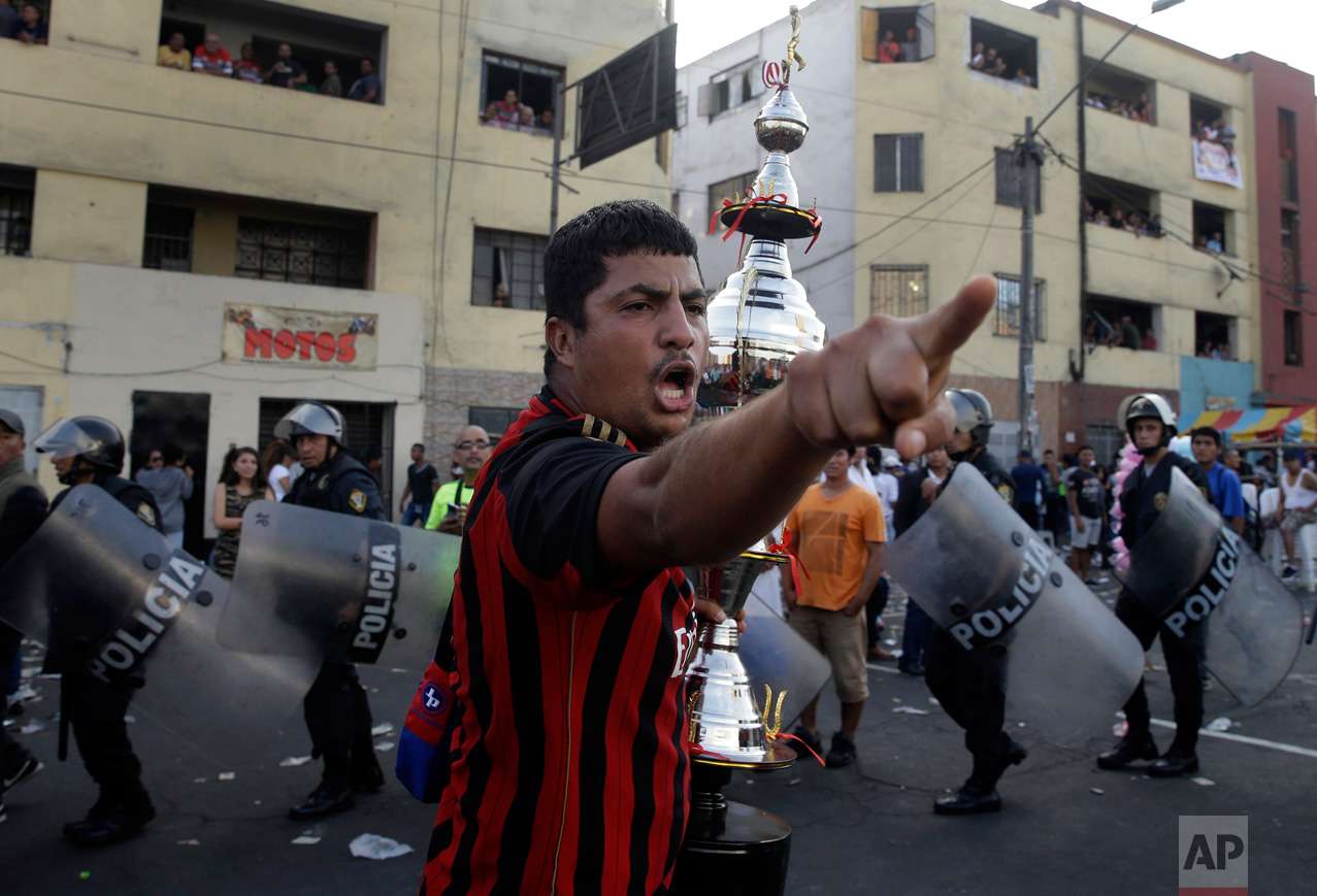  In this Monday, May 1, 2017 photo, a fan of the "Purito Barrios Altos" soccer team yells at rival fans who don't agree with the referee's decision as he runs with his team's trophy after the Little World Cup of Provenir street soccer championship in