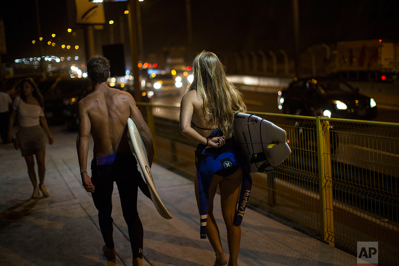  In this Feb. 17, 2017 photo, surfers walk to La Pampilla beach in Lima, Peru. Night surfing apparently came about in Lima because of a dispute with the capital municipality that in 2015 increased the width of a road that runs along the coast. The su