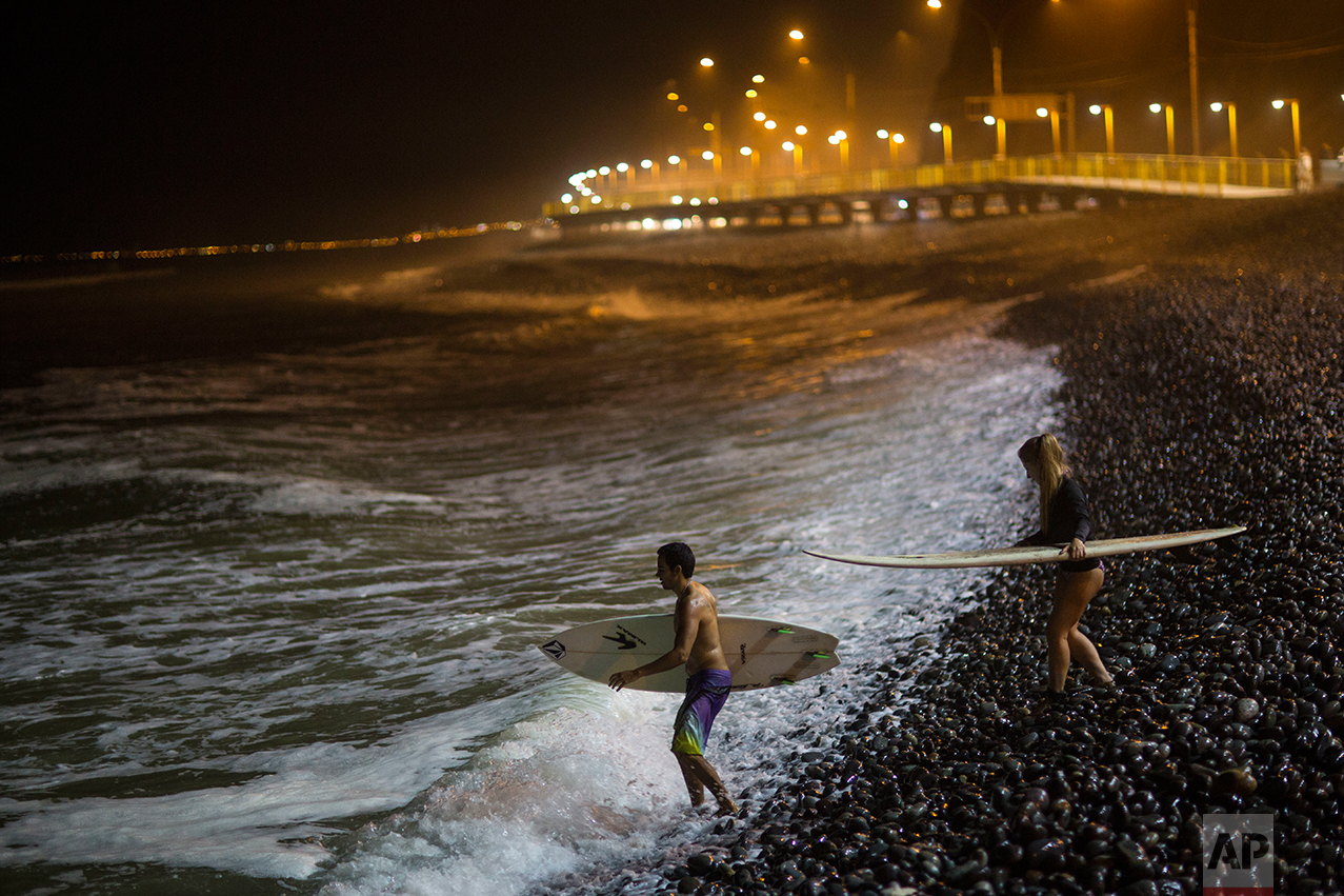  In this March 1, 2017 photo, surfers walk over the rocky shore into the Pacific Ocean at La Pampilla beach in Lima, Peru. The beach attracts fewer than two dozen surfers a night. (AP Photo/Rodrigo Abd) 