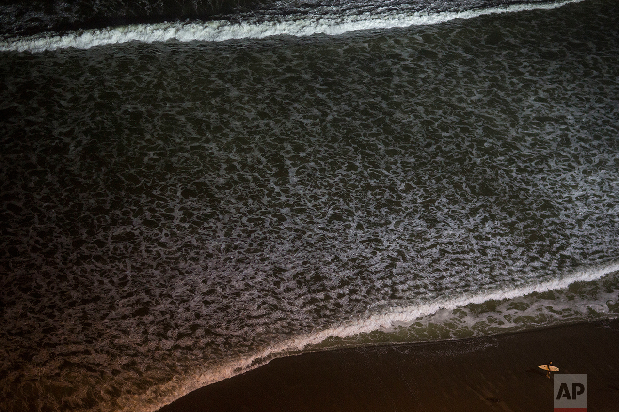  In this March 9, 2017 photo, a surfer walks on the shore of La Pampilla beach, Lima, Peru. The Andean country has decked out the beach with four 1,000-watt lights like those used in soccer stadiums. Placed high above the beach, their lights reach ab