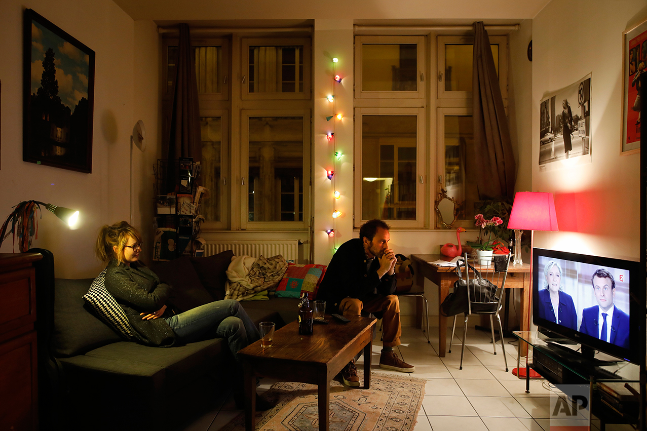  A couple watches a live broadcast television debate with French centrist presidential candidate Emmanuel Macron, right, and far-right candidate Marine Le Pen, in Lyon, central France, Wednesday, May 3, 2017. (AP Photo/Laurent Cipriani) 