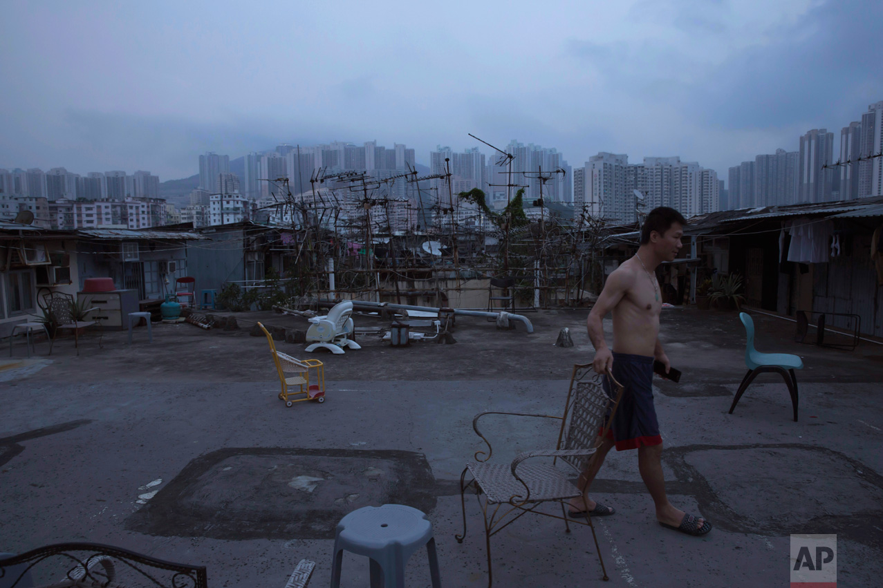  In this Saturday, May 6, 2017 photo, a resident walks outside his illegal rooftop hut located next to a public housing estate, in the background, in Hong Kong. In wealthy Hong Kong, there's a dark side to a housing boom, with hundreds of thousands o
