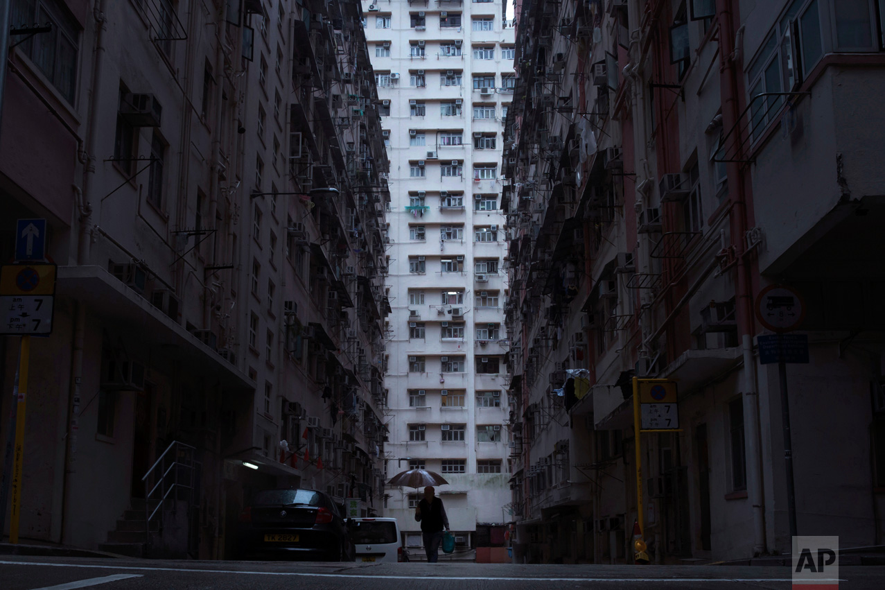  In this Tuesday, April 25, 2017 photo, a man walks in front of a residential and commercial building, center, where the "coffin home" is located in Hong Kong. In wealthy Hong Kong, there's a dark side to a housing boom, with hundreds of thousands of