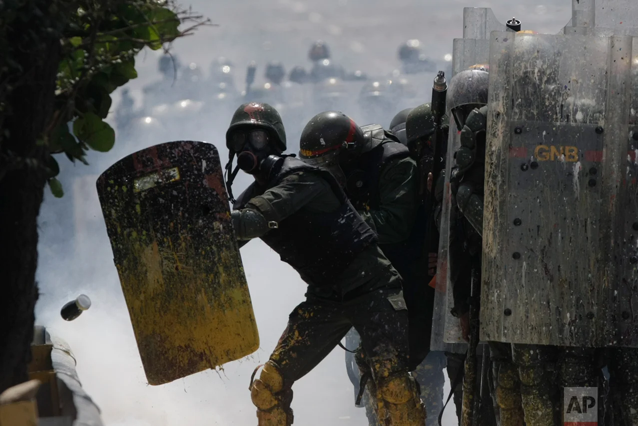 In this May 10, 2017 photo, Bolivarian National Guards shield themselves from a jar filled with fecal matter, thrown by anti-government protesters in Caracas, Venezuela. The government has denounced use of the feces-filled bombs, equating them to a type of biochemical weapon that could spread illnesses. (AP Photo/Fernando Llano)