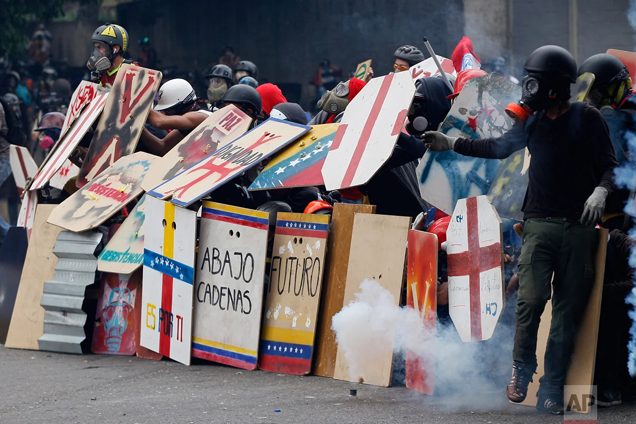 In this May 8, 2017 photo, anti-government protesters use handmade shields as they face off with security forces blocking a student march from reaching the Education Ministry in Caracas, Venezuela. Hundreds of thousands have taken to the streets to castigate President Nicolas Maduro's administration, which they claim has become a dictatorship responsible for triple-digit inflation, skyrocketing crime and crippling food shortages. (AP Photo/Ariana Cubillos)
