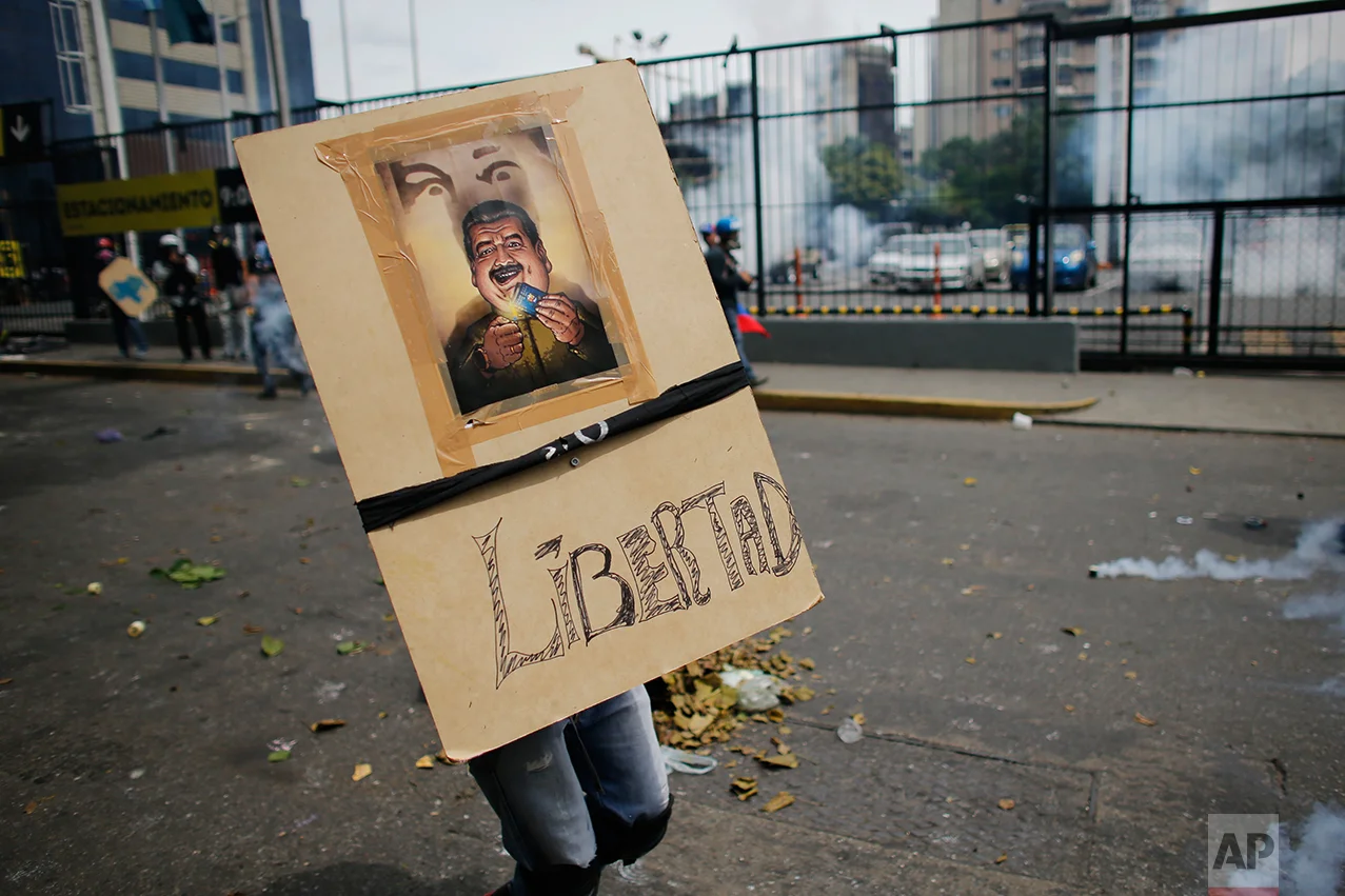 In this May 8, 2017 photo, an anti-government demonstrator carries a homemade shield depicting Venezuela's President Nicolas Maduro burning the country's constitution, and with a message that reads in Spanish: "Freedom" in Caracas, Venezuela. Protesters mass behind wooden shields bearing medieval decorations or images of the South American nation's blue constitution book, which Maduro wants to rewrite. (AP Photo/Ariana Cubillos)