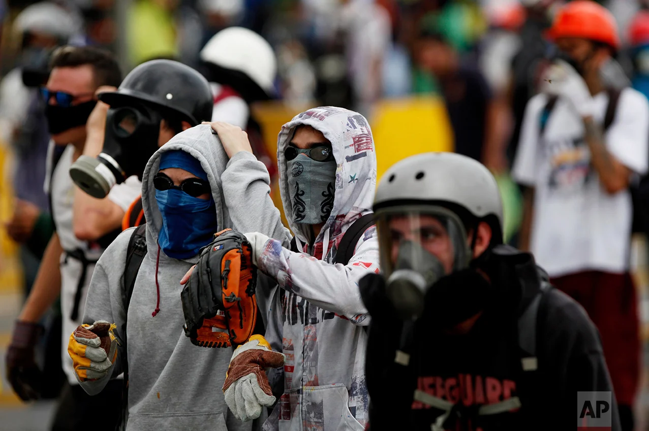 In this May 8, 2017 photo, a demonstrator wears a baseball glove to catch tear gas canisters launched by Bolivarian National Guards during an anti-government protest in Caracas, Venezuela. Some of the canisters land close to protesters, and the opposition contends several demonstrators have died after being struck, though official causes of death have not been released. (AP Photo/Fernando Llano)