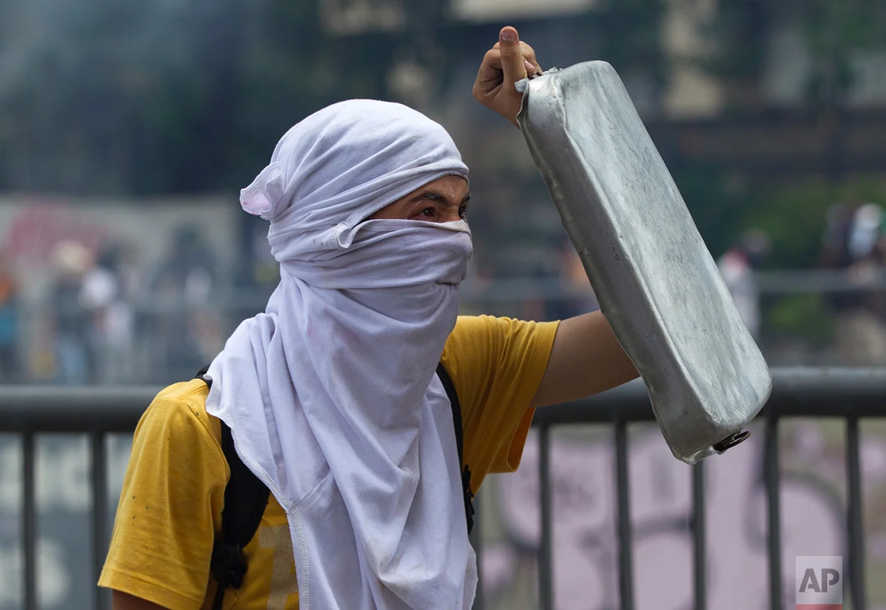 In this April 8, 2017 photo, an anti-government demonstrator shields himself with a cooking pan during clashes with Bolivarian National Guards in Caracas, Venezuela. At least 38 people have been killed and hundreds injured in protests that erupted after the Supreme Court issued a ruling March 29 nullifying the opposition-controlled National Assembly, a decision it later reversed amid a storm of international criticism and outrage among Venezuelans. (AP Photo/Ariana Cubillos)