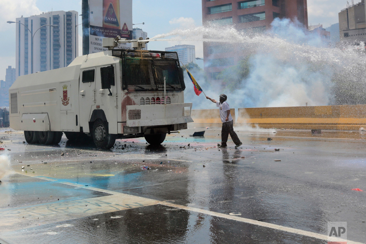 An anti-government protester points a Venezuelan flag at a security forces in a water canon vehicle during an opposition march in Caracas, Venezuela, on Wednesday, May 10, 2017. Opponents of President Nicolas Maduro attempted to march to the Supreme Court to protest its decision to gut the opposition-controlled congress of its powers _ a ruling that was quickly rescinded under a barrage of international criticism but that set off weeks of political unrest that have left some three dozens killed. (AP Photo/Fernando Llano)