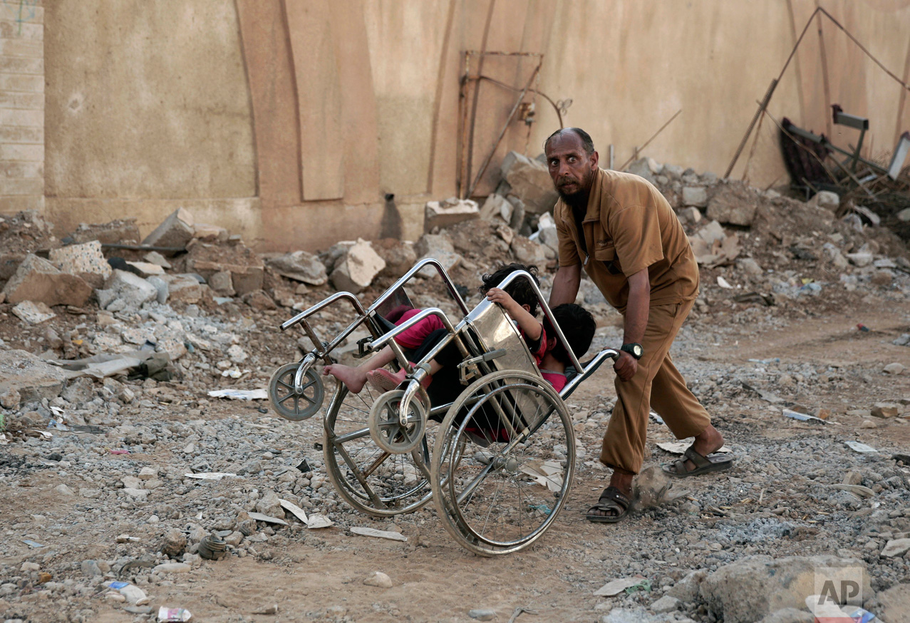 A man pushes two children in a wheelchair as they flee heavy fighting between Islamic State militants and Iraqi special forces in Mosul, Iraq, Wednesday, May 10, 2017. Iraqi army, federal police and special forces, backed by the U.S.-led coalition, are slowly retaking territory in Mosul where IS remains in control of a small cluster of neighborhoods in the city's western half. (AP Photo/Maya Alleruzzo)