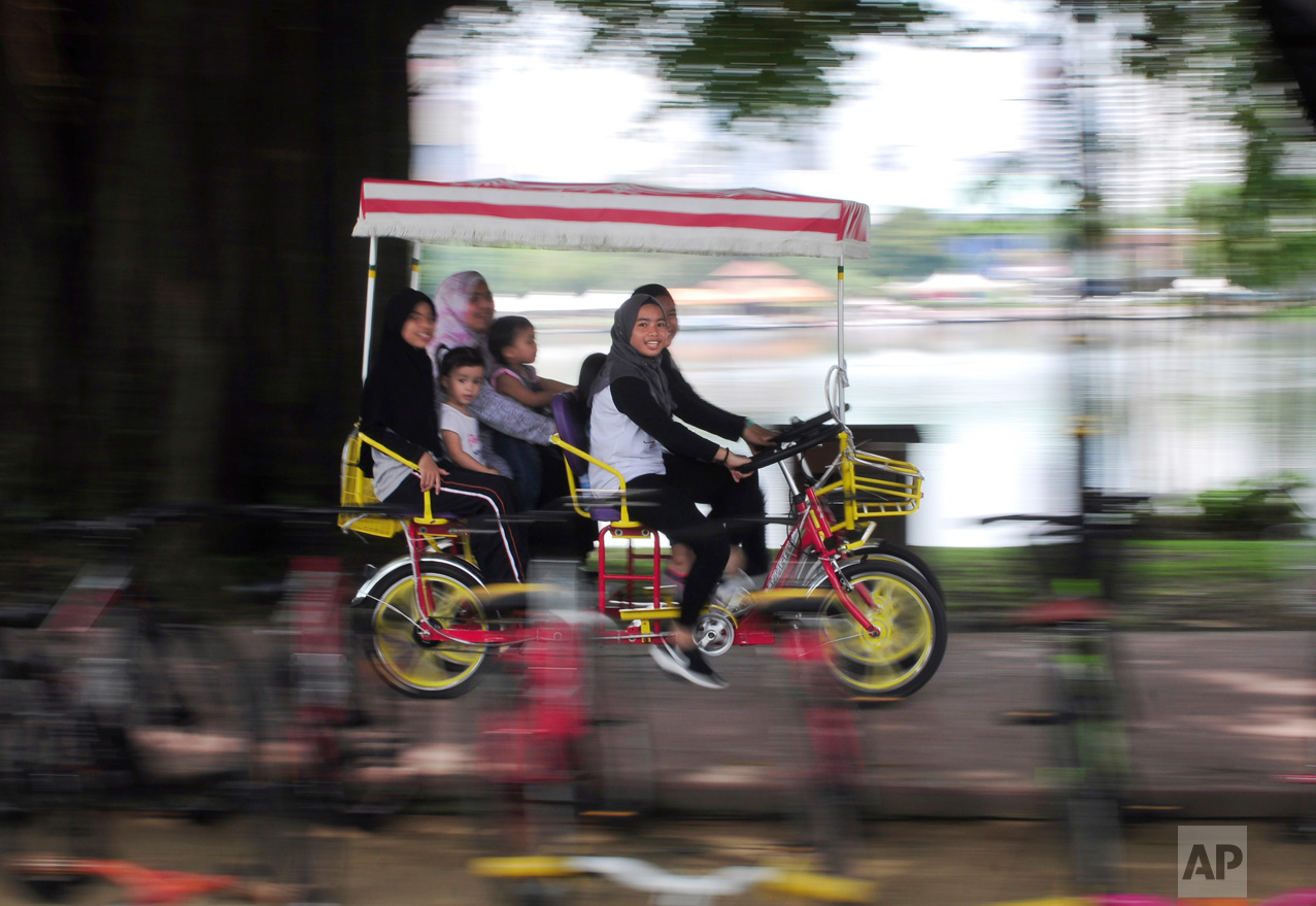 A family rides a cycle together at the Titiwangsa lake gardens in Kuala Lumpur, Malaysia, on Saturday, May 6, 2017. Titiwangsa lake gardens is a recreational park with a large lake located in the north-eastern fringe of Kuala Lumpur city center. (AP Photo/Daniel Chan)