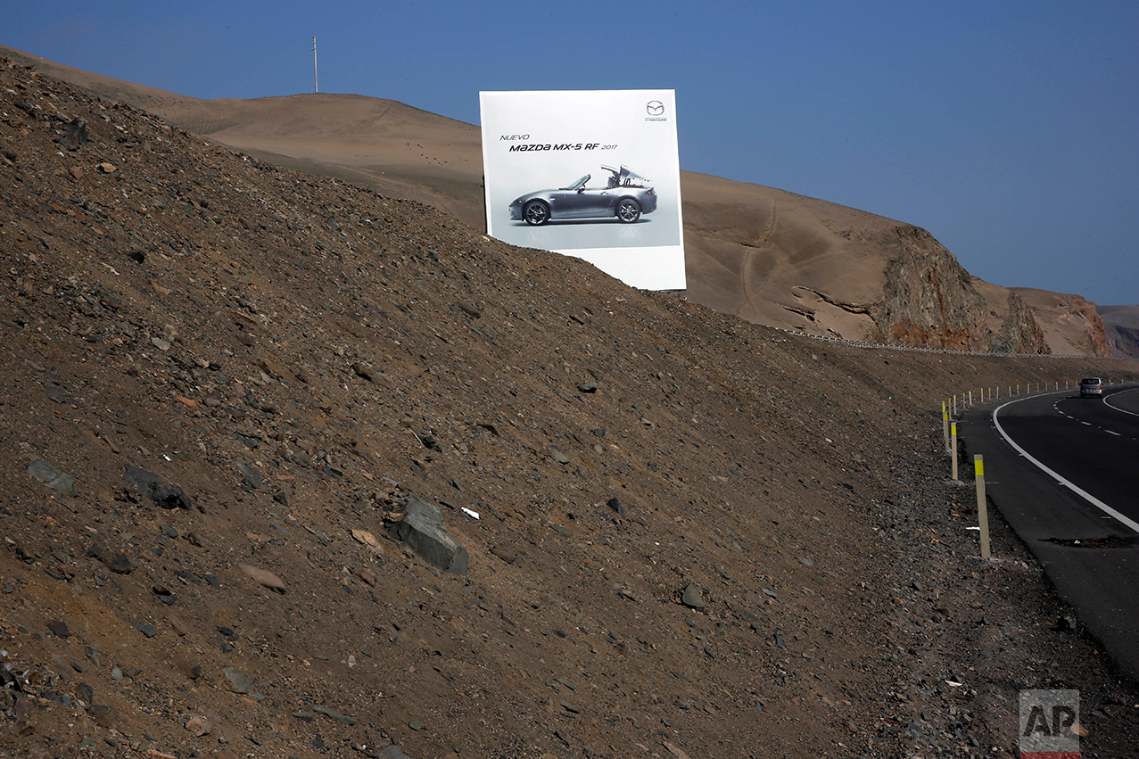  In this May 5, 2017 photo, a billboard advertising a Mazda sports car stands along the Pan American Highway on the south side of Lima, Peru. Standing on the brown, barren landscape, the billboards advertise other products the people living in this a
