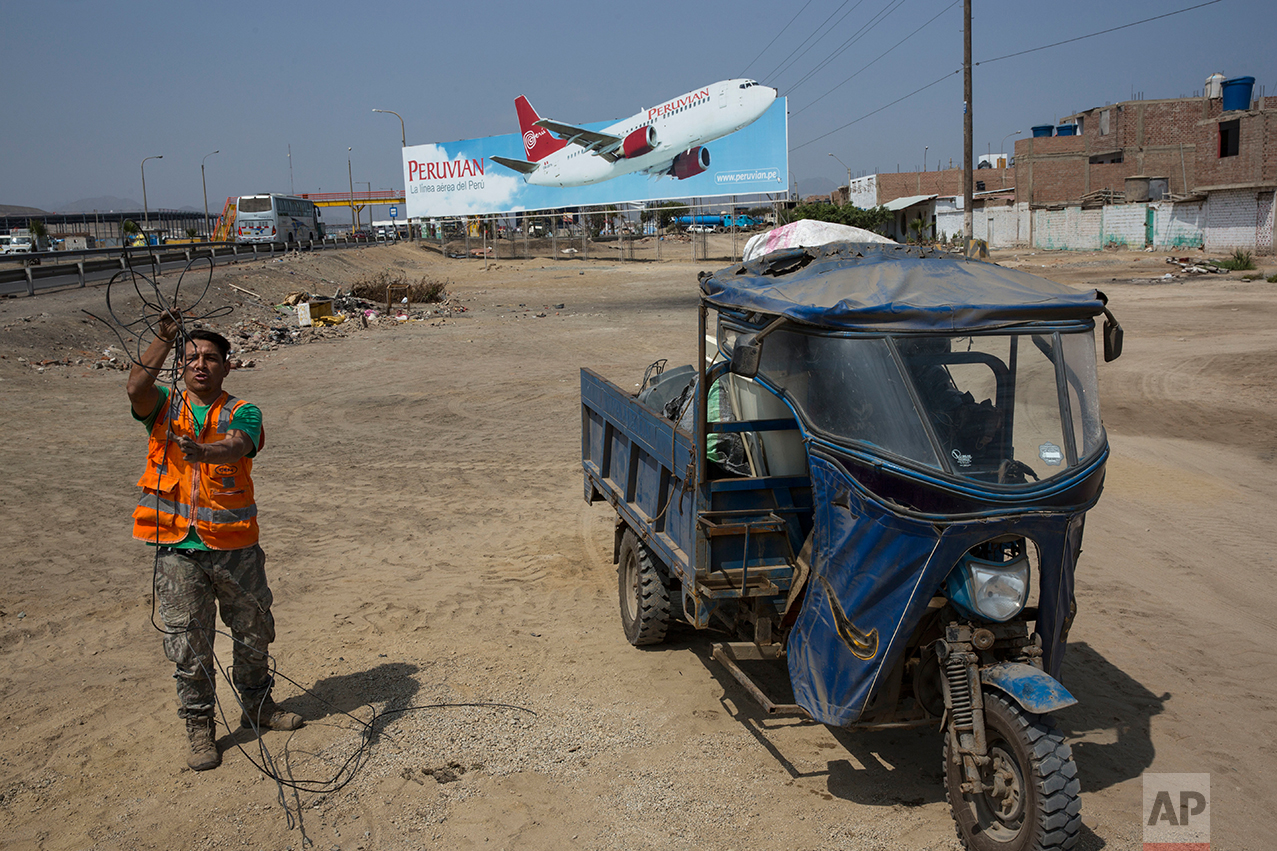  In this May 5, 2017 photo, a man collects cables for resale, along with other recyclable objects, along the Pan American Highway where a billboard advertises a local airline on the south side of Lima, Peru. Below the billboards are cannibalized cars