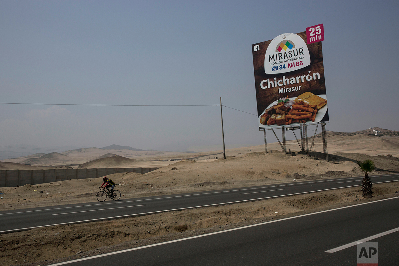  In this May 5, 2017 photo, a cyclist passes a billboard advertising a restaurant along the Pan American Highway on the south side of Lima, Peru. Below the billboards are cannibalized cars, piles of used brick and white crosses marking the places whe