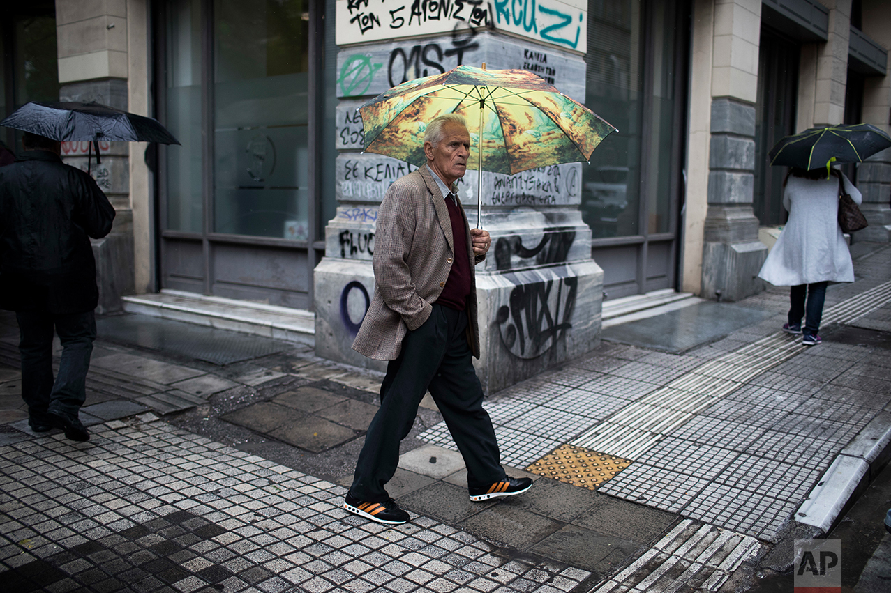  In this Thursday, May 18, 2017 photo an elderly man holding an umbrella walks during rainfall in central Athens. (AP Photo/Petros Giannakouris) 